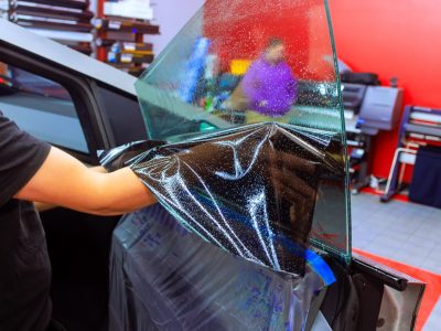 Technician carefully installs window tint film on vehicle in a well equipped work car shop.